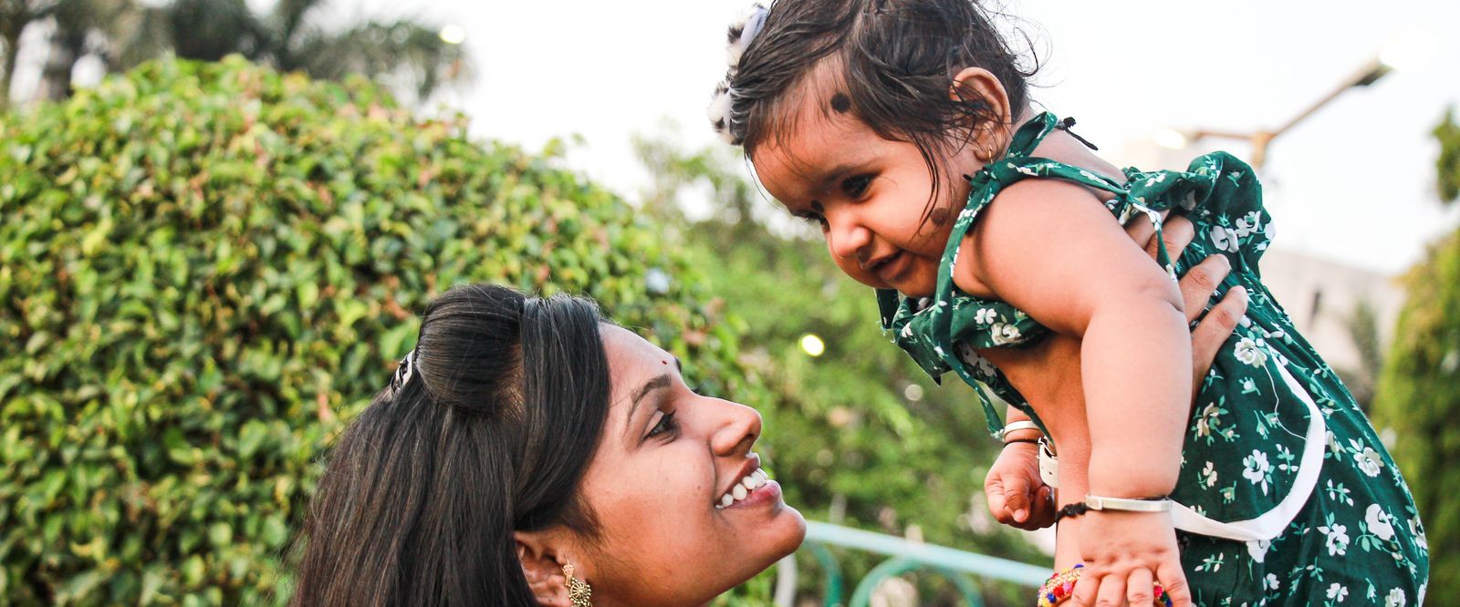 A mother laughing as she lifts her small daughter up in a garden