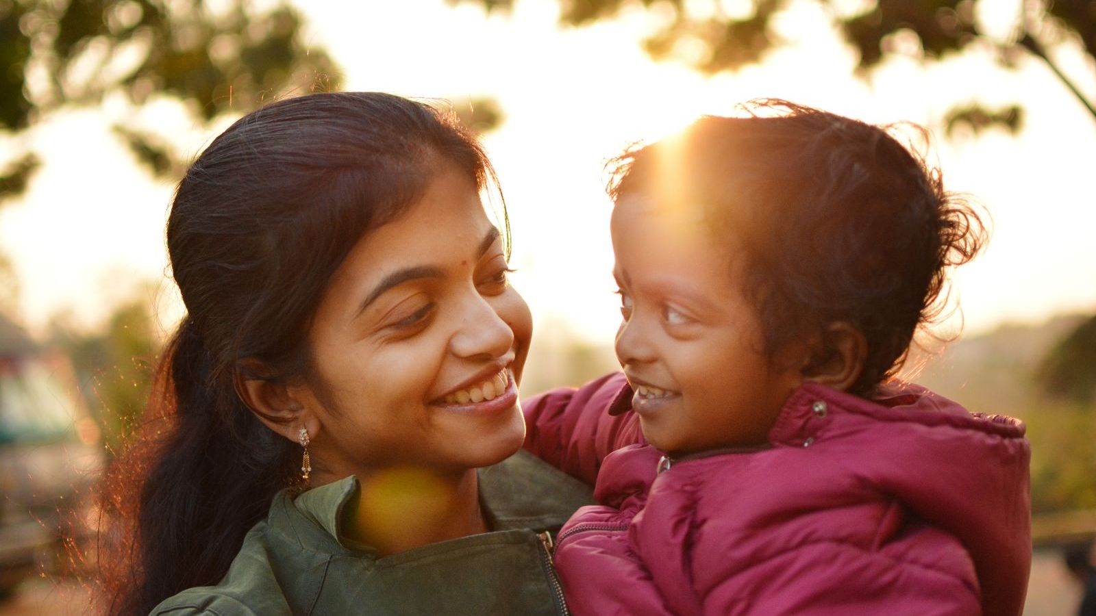 A mother and her small child laughing together outdoors at sunset